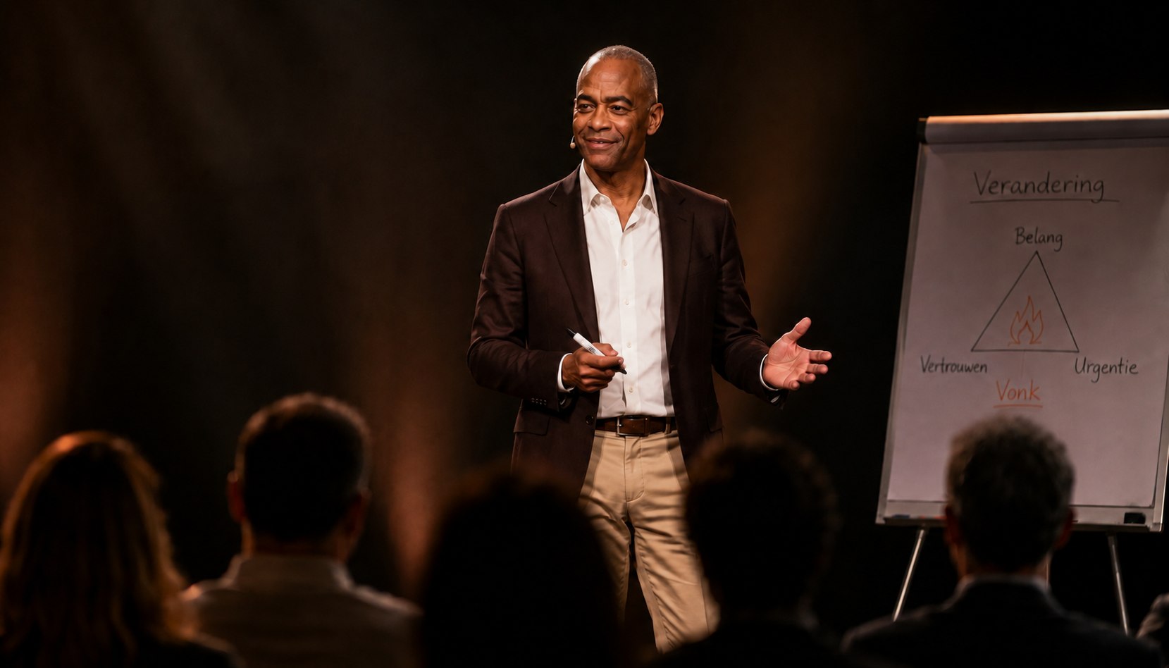 Greg Trinidad legt de Vuurdriehoek uit op een podium: belang, vertrouwen en urgentie, met de vonk eronder